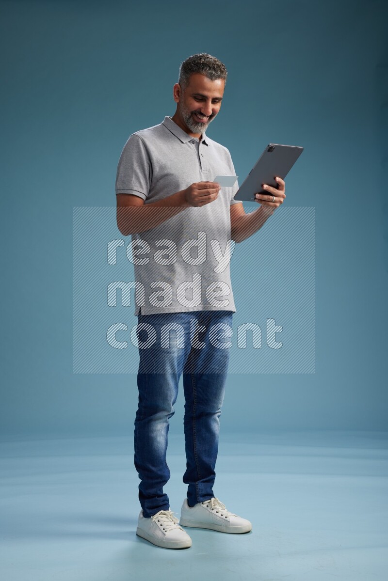 Man Standing holding ATM while working on tablet on blue background