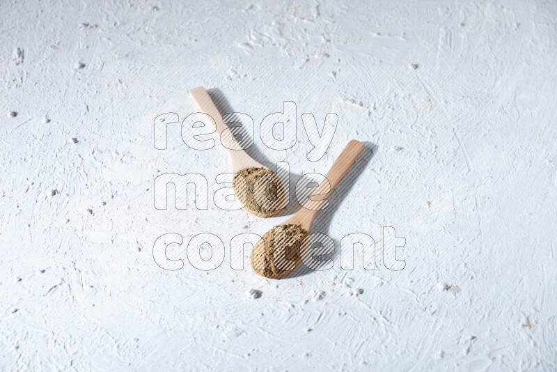 Wooden spoons full of allspice powder and allspice whole balls spreaded on a textured white flooring