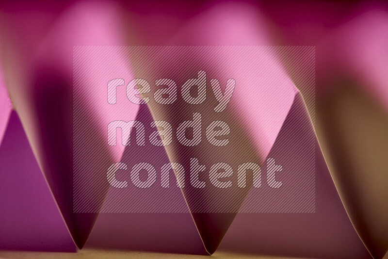 A close-up abstract image showing sharp geometric paper folds in pink gradients and warm tones