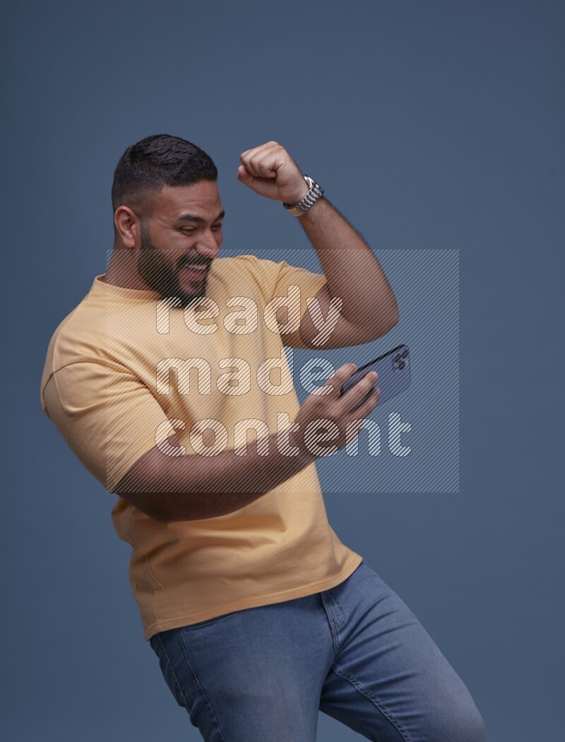 رجل يرتدي بنطال ازرق جينز وقميص اصفر بأكمام قصيره يلعب في جواله