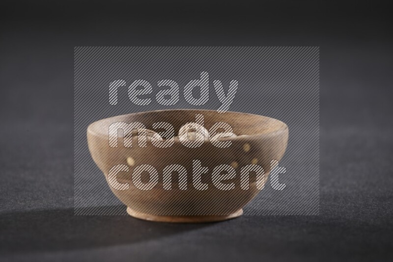 A wooden bowl full of whole nutmeg seeds on a black flooring