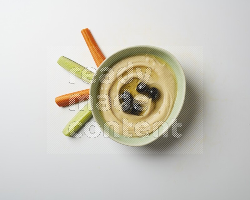 Hummus in a green plate garnished with black olives on a white background