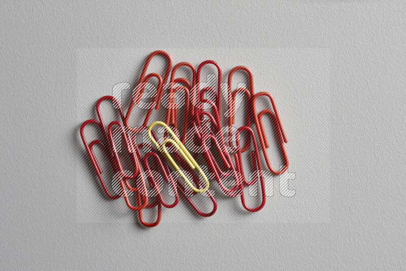 A bunch of red paper clips with a different colored paper clip in the center on grey background
