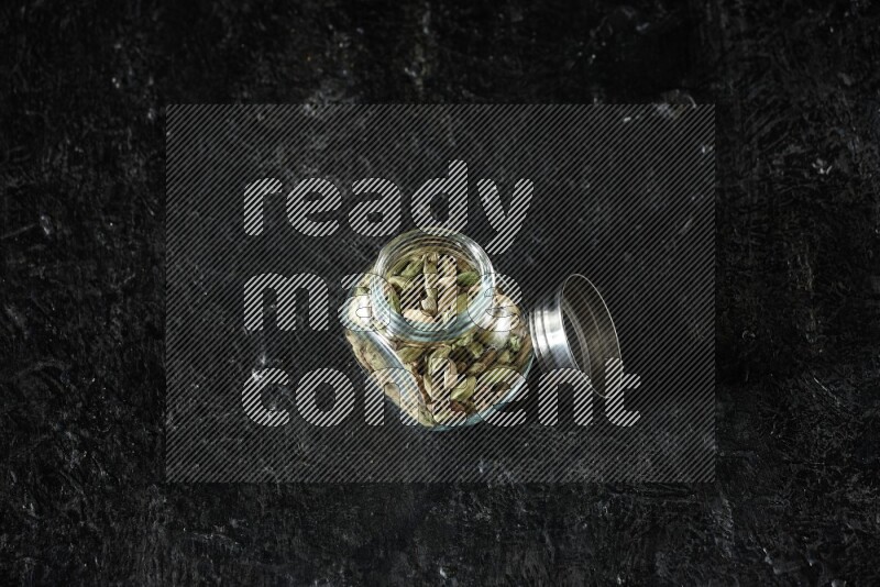 وعاء بهارات زجاجي ممتلئ بحبوب الهيل على خلفية سوداء