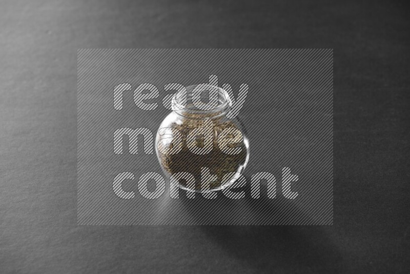 A glass spice jar full of cumin on black flooring