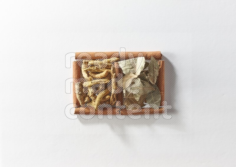 2 squares of cinnamon sticks full of turmeric fingers and bay laurel leaves on white flooring