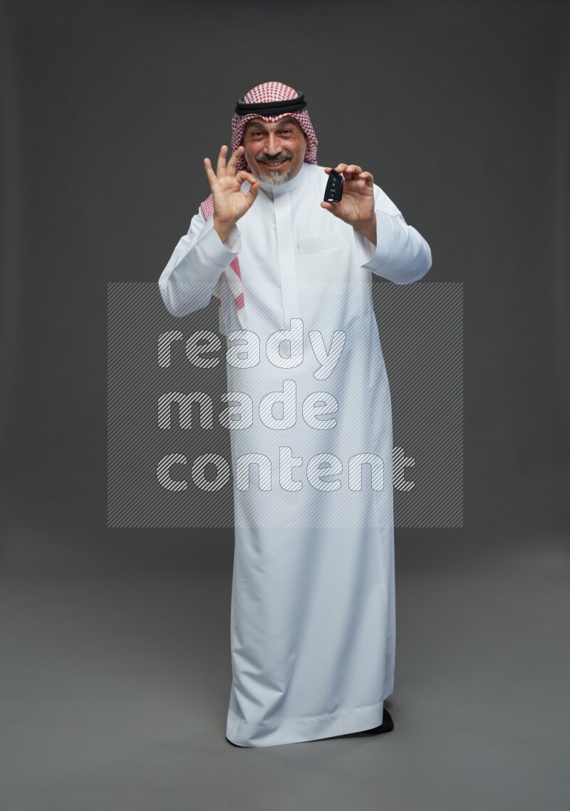 Saudi man with shomag Standing holding car key on gray background