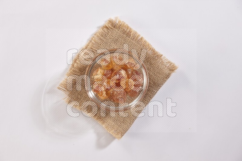 A glass bowl full of gum arabic on a burlap piece on white flooring