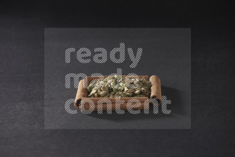 أربعة من أعواد القرفة مكونة شكل مربع بداخلها حبوب الهيل علي خلفية سوداء