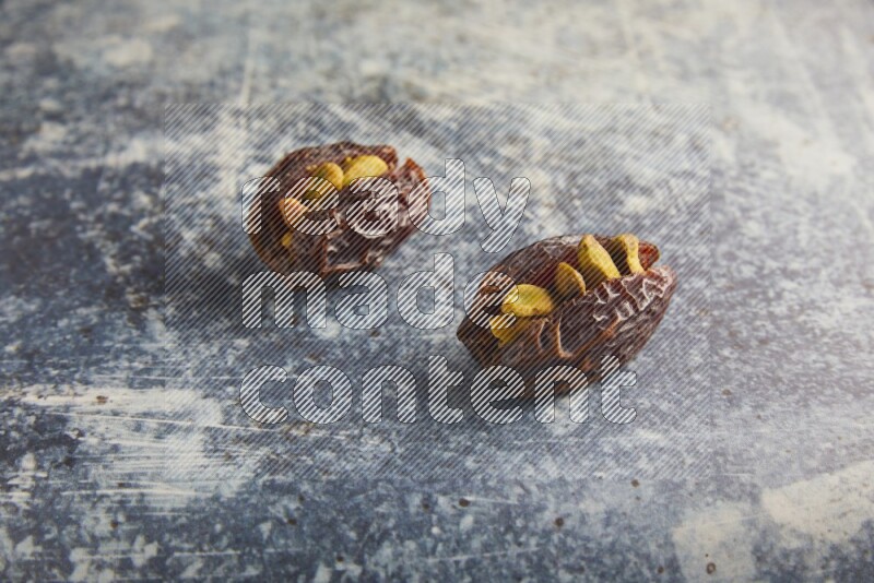 two pistachios stuffed madjoul dates on a rustic blue background