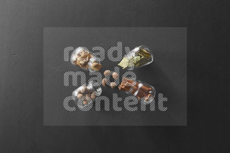 أوراق الغار وزنجبيل مجفف وقرفة وجوزة الطيب في أوعية زجاجية علي خلفية سوداء