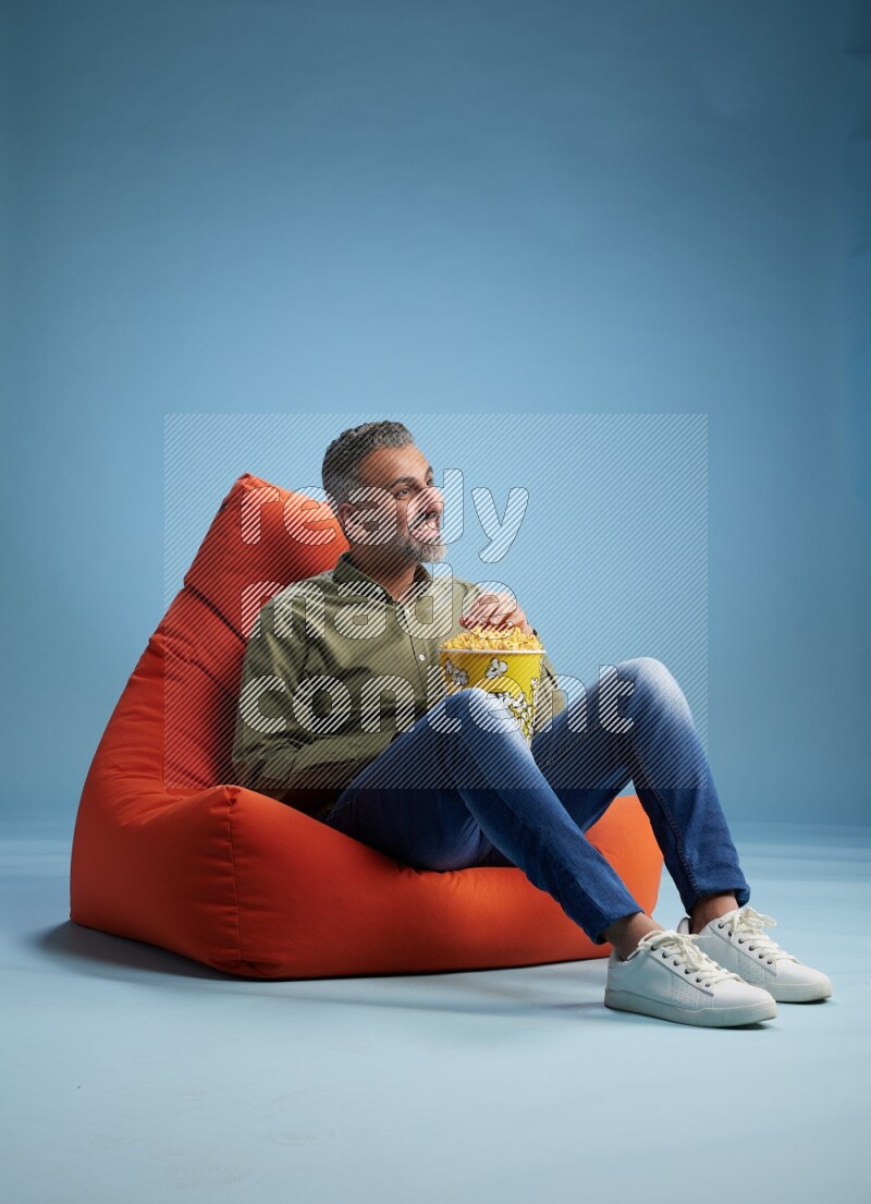 A man sitting on an orange beanbag and eating popcorn