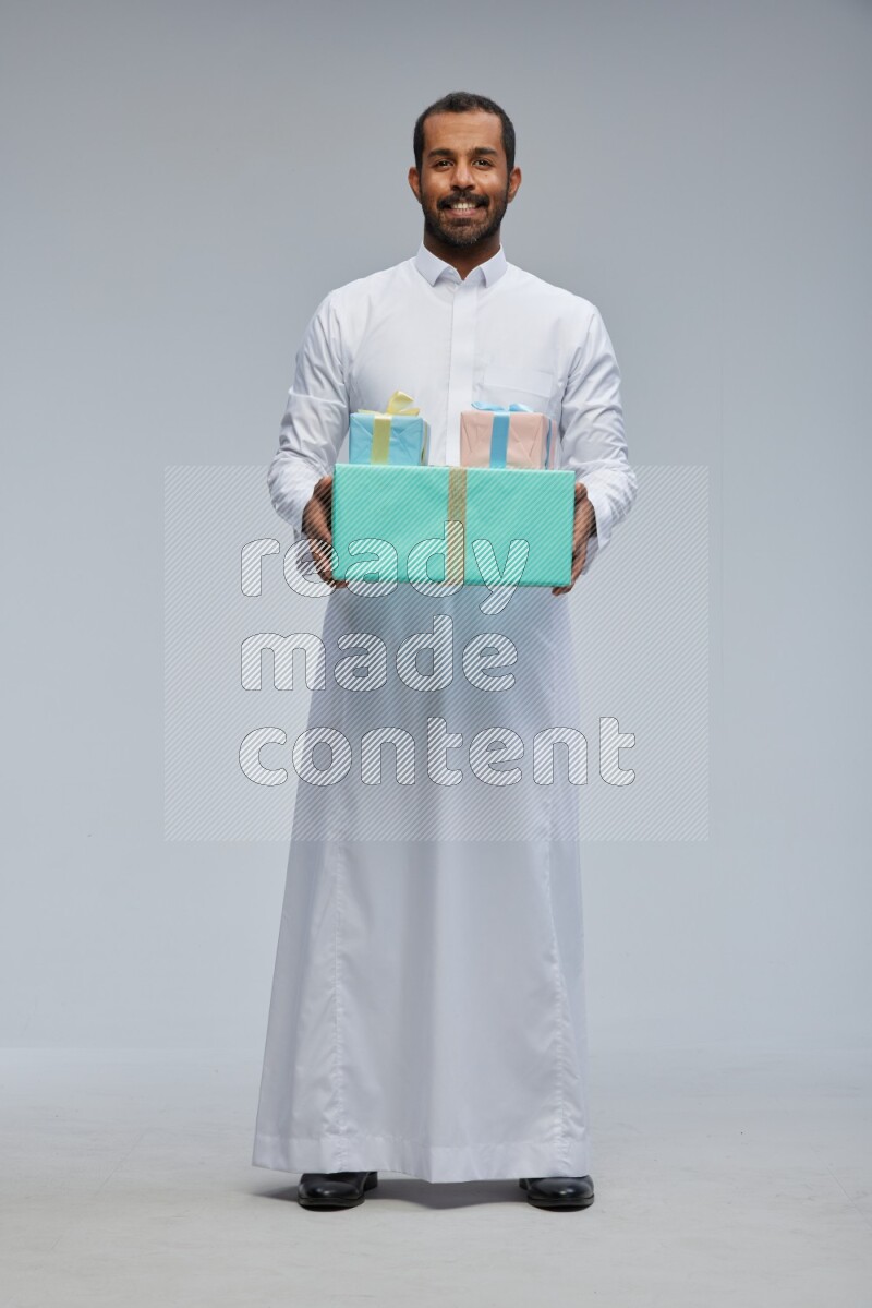 Saudi man Wearing thob standing holding gift box on Gray background