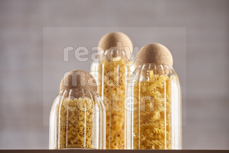 Raw pasta in glass jars on beige background