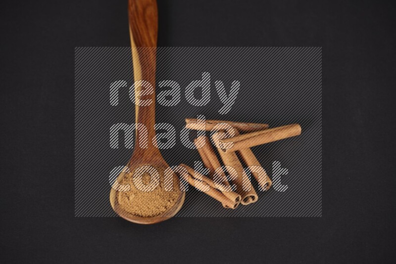 Cinnamon powder in a wooden ladle spoon beside it cinnamon sticks on the flooring on black background in different angles