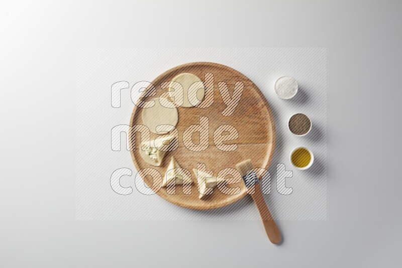 two closed sambosas and one open sambosa filled with cheese while salt, black pepper and oil with oil brush aside in a wooden dish on a white background