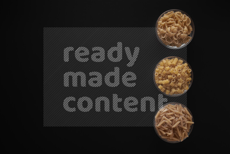 Different pasta types in 3 glass bowls on black background