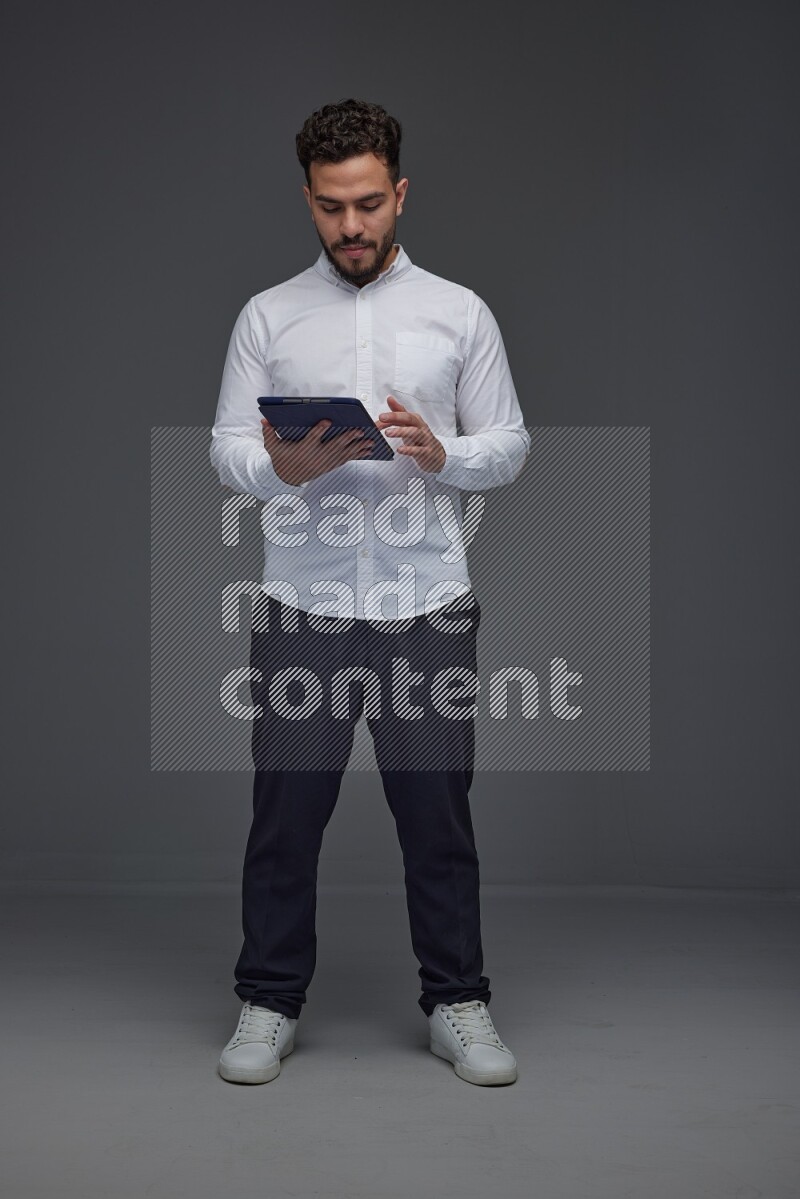 A man wearing smart casual standing and using his tablet eye level on a gray background