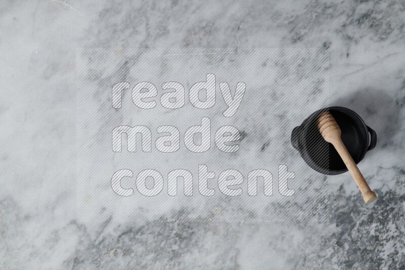 وعاء فخاري أسود مع ملعقة عسل خشبية بداخله على خلفية من الرخام الرمادي