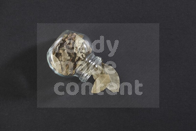 وعاء زجاجي ممتلئ بأوراق الغار والوعاء مقلوب وبعض الأوراق متناثرة خارجه علي خلفية سوداء