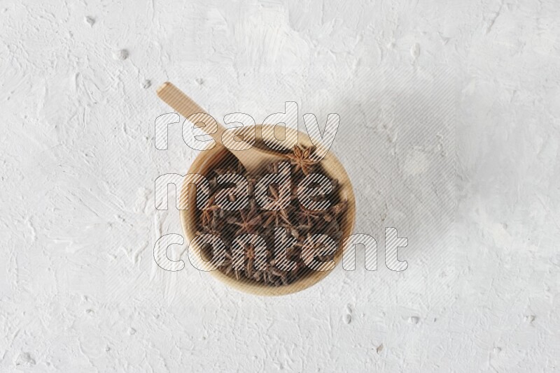 Star anise in a wooden bowl with a wooden spoon in it on white background