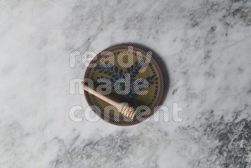 Decorative pottery plate with wooden honey dipper in it on grey marble background