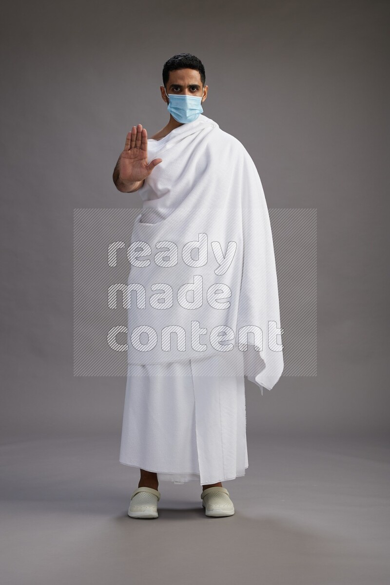 A man wearing Ehram with face mask Standing Interacting with the camera on gray background