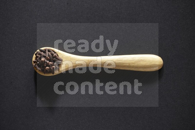 A wooden spoon full of cloves on a black flooring