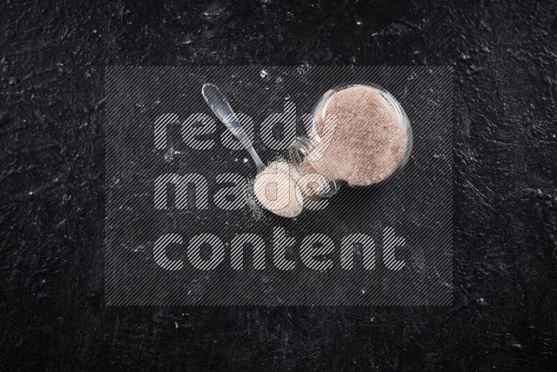 A glass jar full of fine himalayan salt on black background