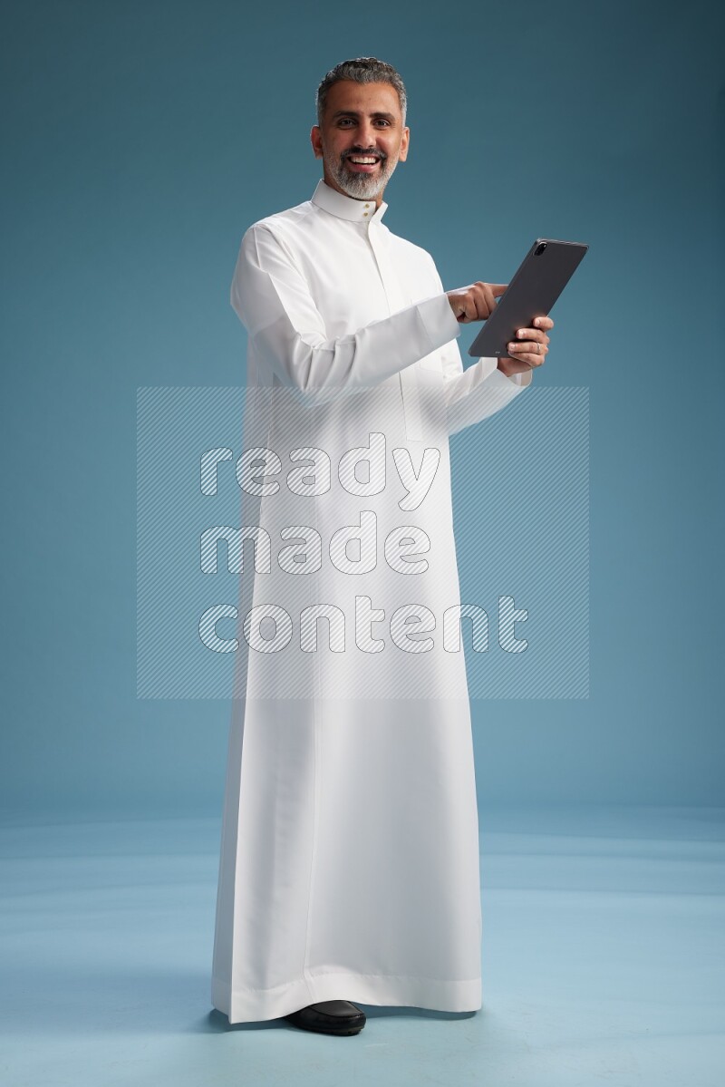 Saudi man waring thob with tablet on blue background