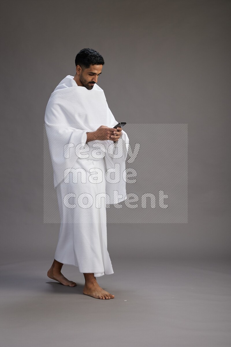 A man wearing Ehram Standing texting on phone on gray background