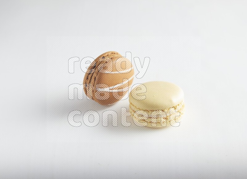 45º Shot of of two assorted Brown Irish Cream, and Yellow Vanilla macarons on white background