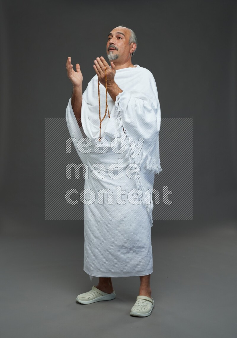 A man wearing Ehram Standing dua'a on gray background