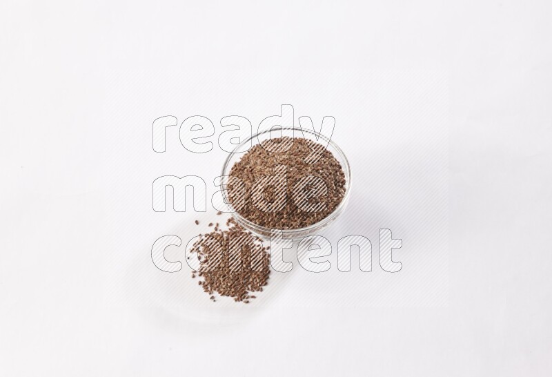 A glass bowl full of flax seeds surrounded by flax seeds on a white flooring