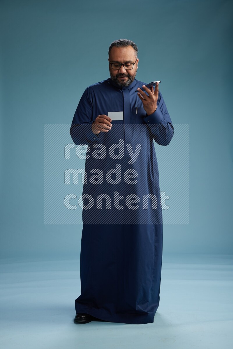 Saudi Man without shimag Standing holding ATM while talking on phone on blue background