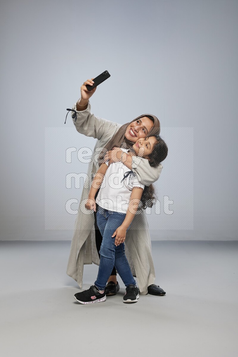 A girl standing taking selfie with her mother on gray background