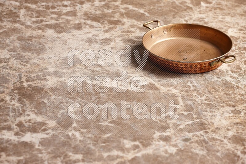 A small copper pan on beige marble background