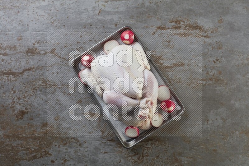 whole Raw chicken on a small oven trey direct on a rustic grey background