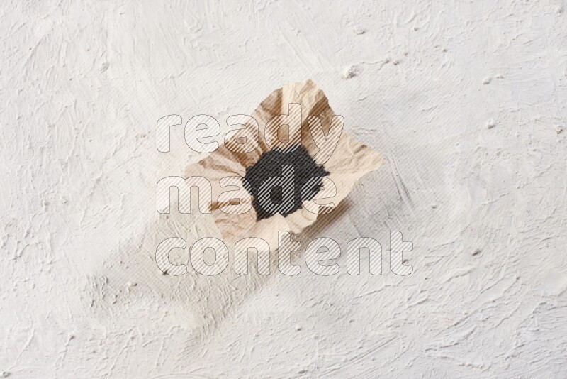 A crumpled piece of paper full of black seeds on a textured white flooring