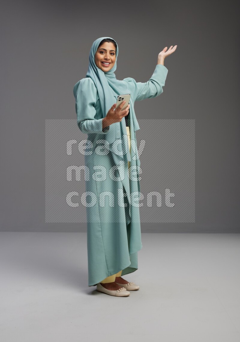 Saudi Woman wearing Abaya standing texting on phone on Gray background