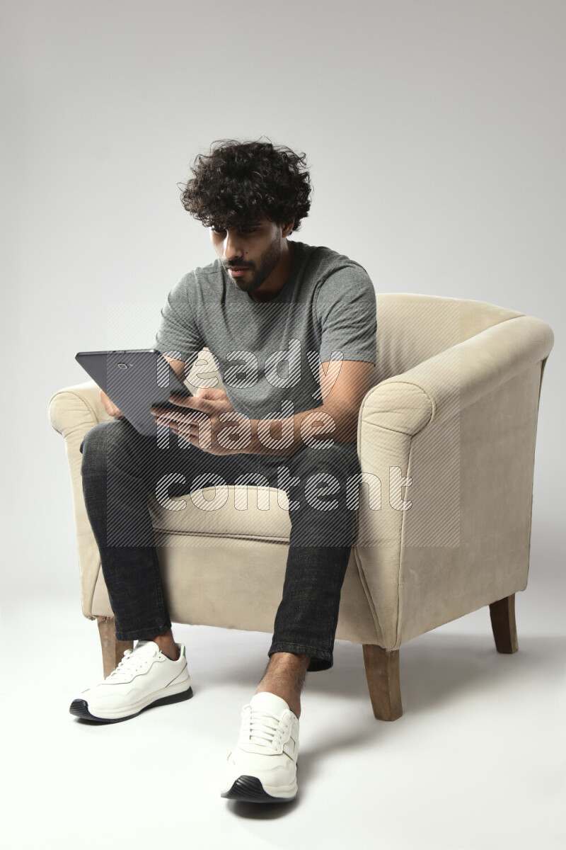 A man wearing casual sitting on a chair browsing on a tablet on white background