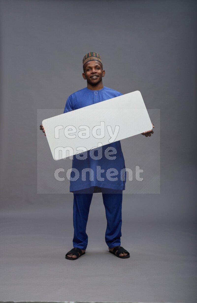 Man wearing Nigerian outfit standing holding board on gray background