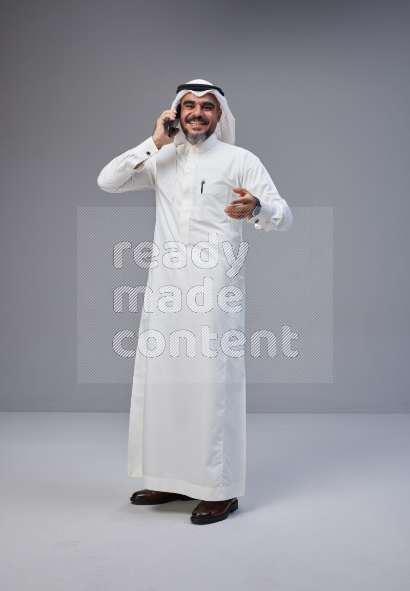 Saudi man Wearing Thob and white Shomag standing talking on phone on Gray background