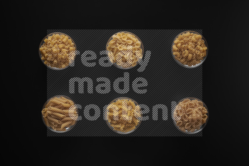 Different pasta types in 6 glass bowls on black background