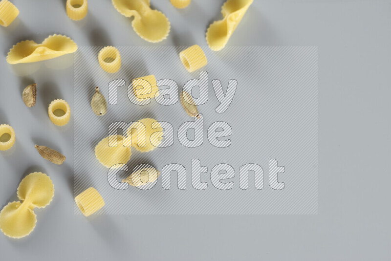 Raw pasta with different ingredients such as cherry tomatoes, garlic, onions, red chilis, black pepper, white pepper, bay laurel leaves, rosemary, cardamom and mushrooms on light blue background