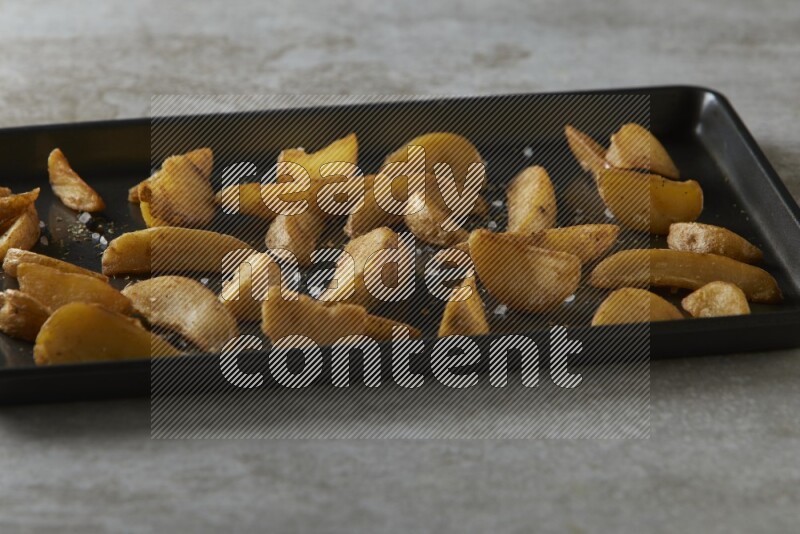 wedges potato in a black stainless steel rectangle tray on grey textured counter top