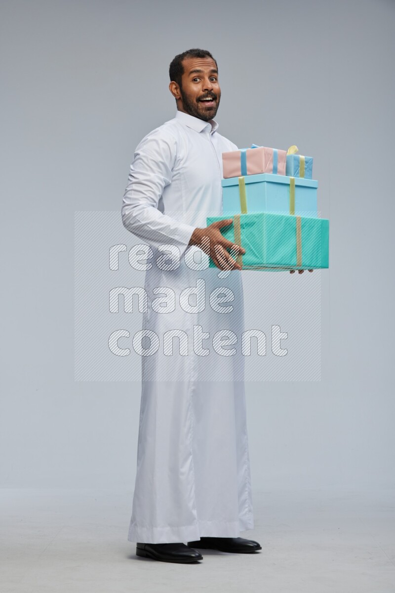 Saudi man Wearing thob standing holding gift box on Gray background