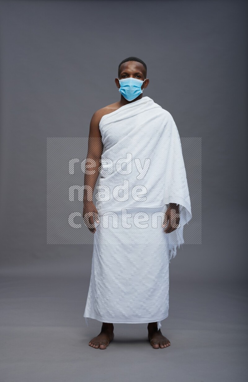 A man wearing Ehram with face mask Standing Interacting with the camera on gray background