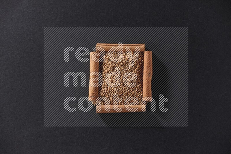 A single square of cinnamon sticks full of mustard seeds on black flooring