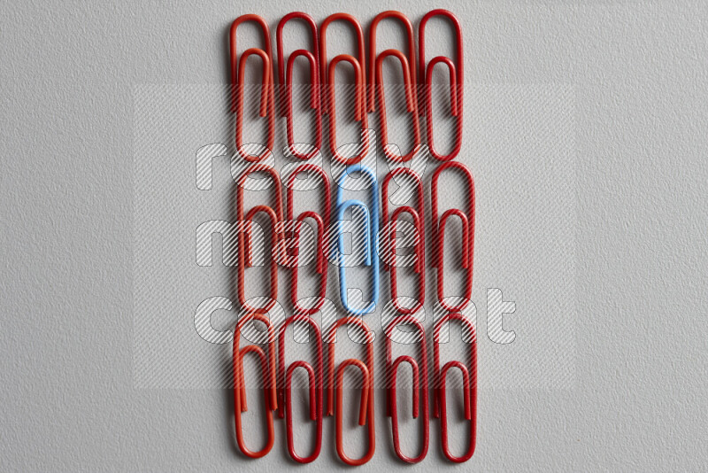 A bunch of red paper clips with a different colored paper clip in the center on grey background